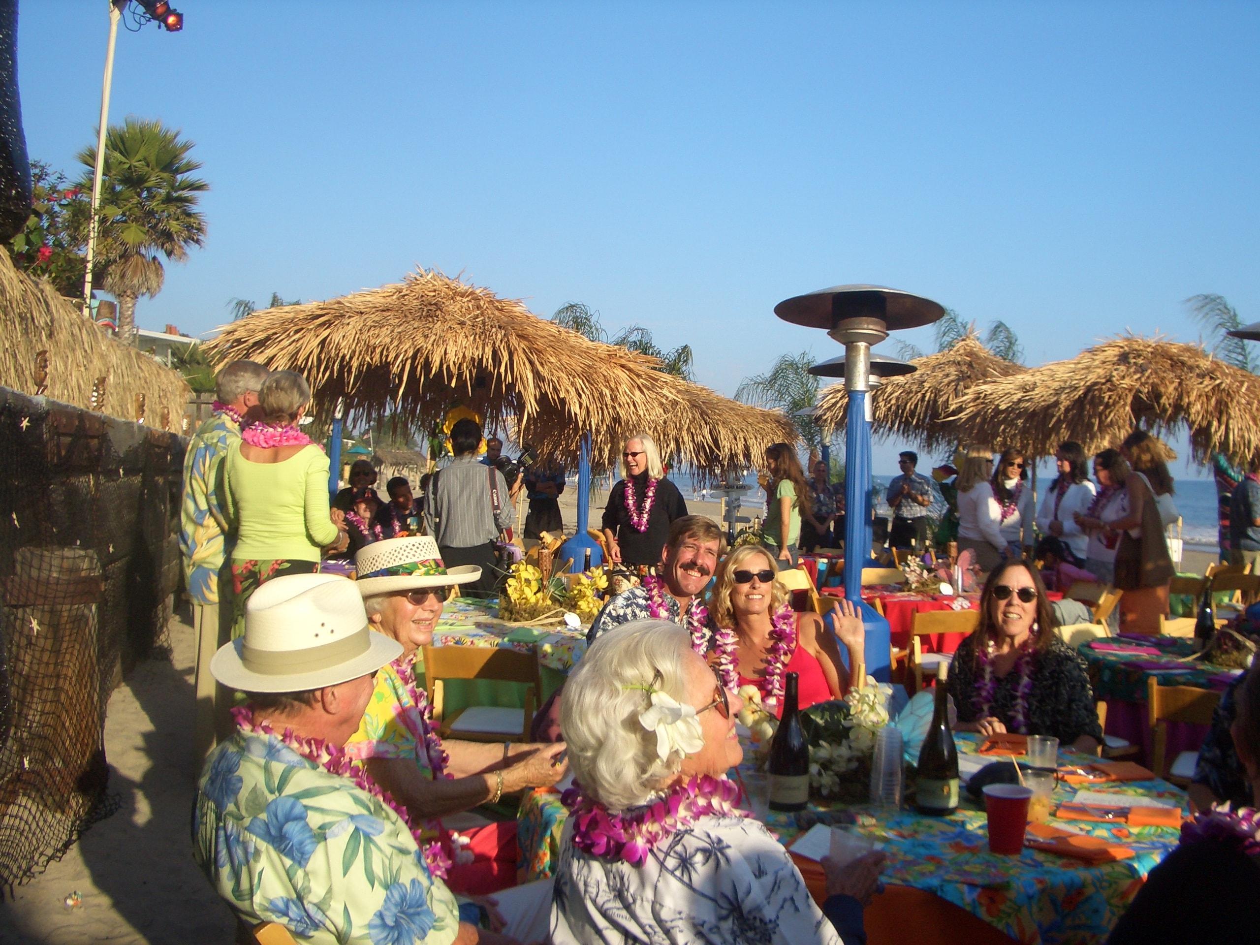 Catering staff in Hawaiian attire serving under thatched palapa on the beach with tiki torches in Los Angeles, CA