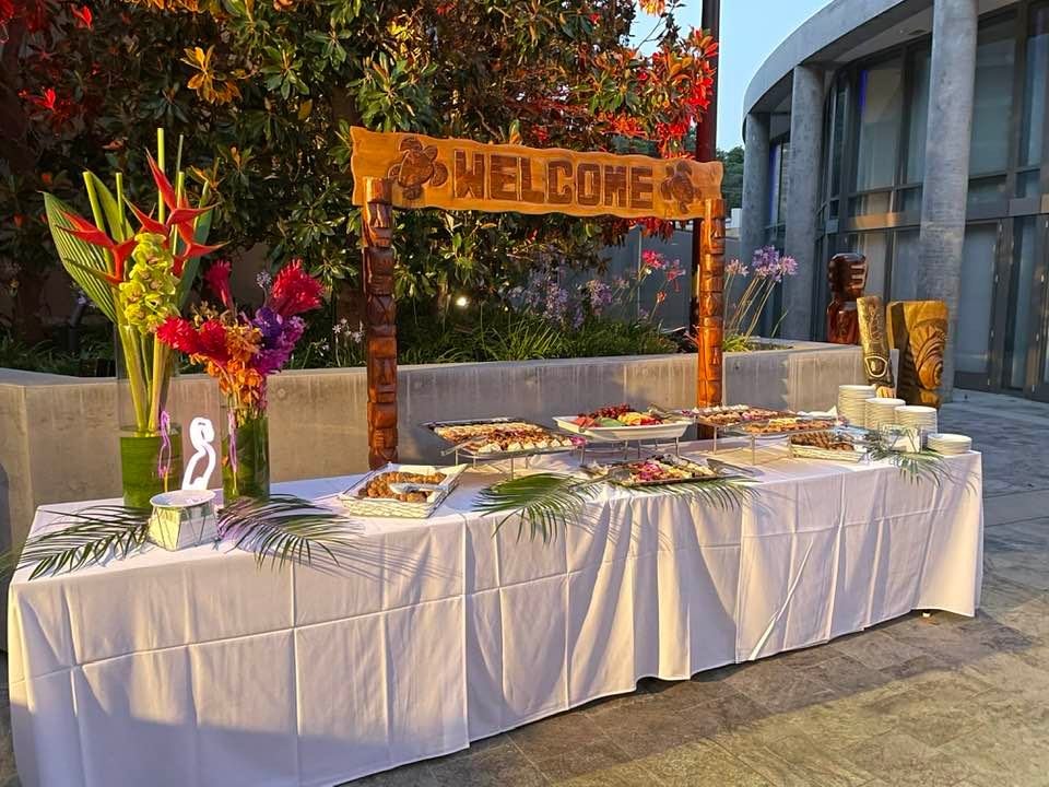 Welcome catering table with carved arch, tropical floral arrangements, and full Hawaiian food spread in Las Vegas