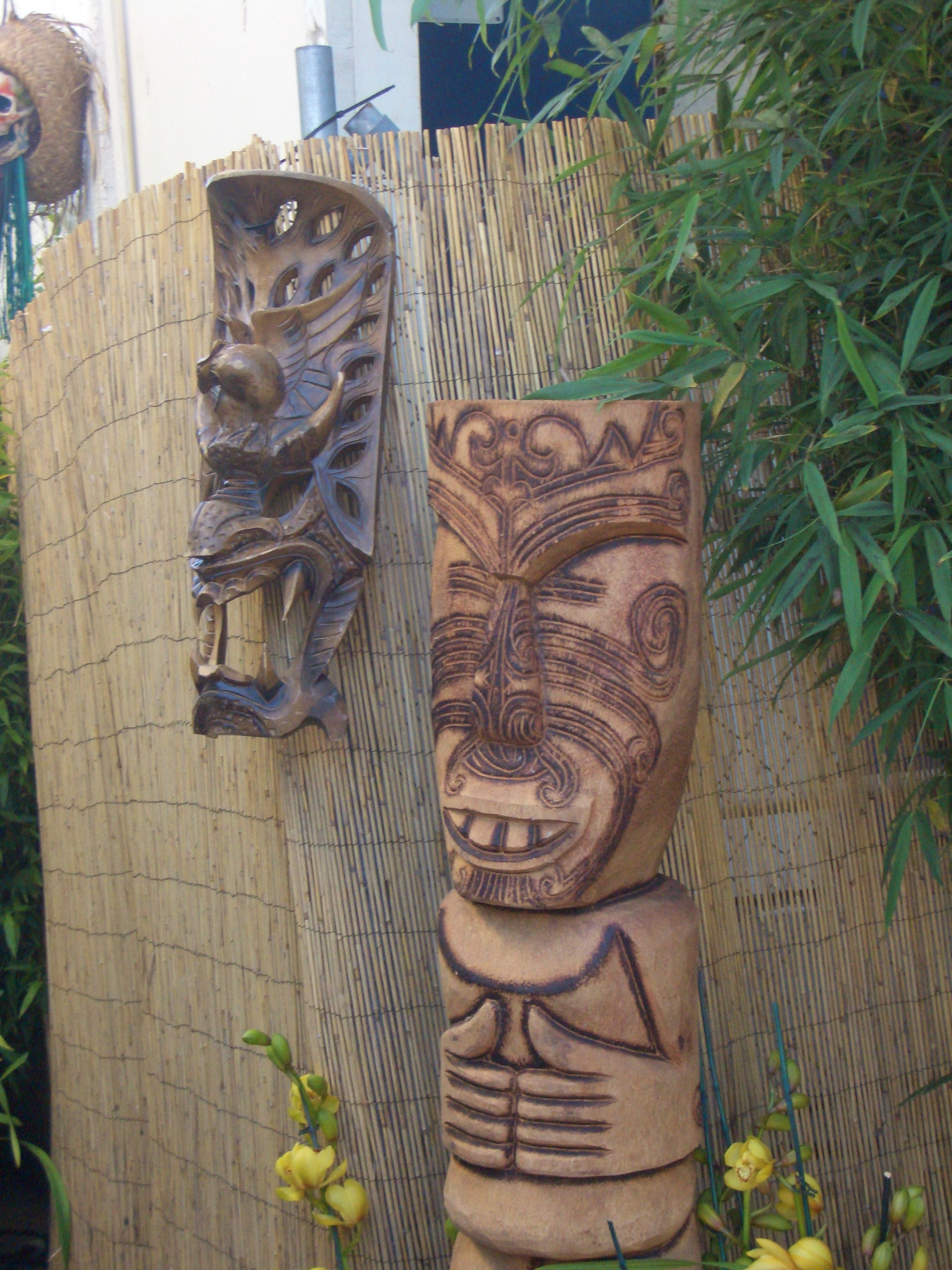 Carved wooden tiki statues and tribal panels on bamboo fence with tropical foliage at a Las Vegas luau